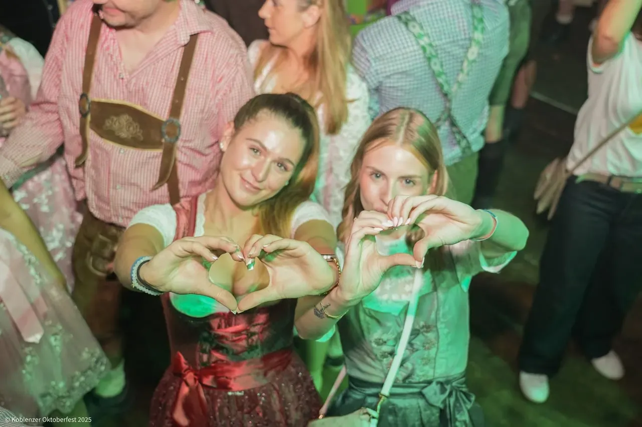 Zwei Gäste im Dirndl formen Herzen mit den Händen im Festzelt